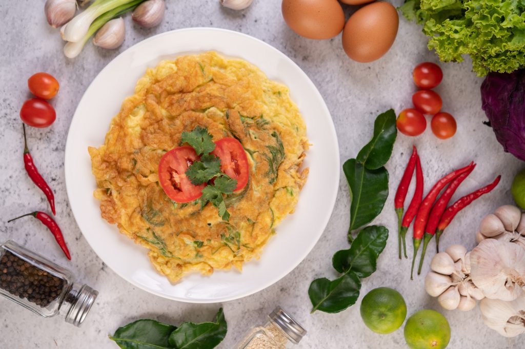 Omelet In A White Plate Garnished With Tomatoes And Coriander.